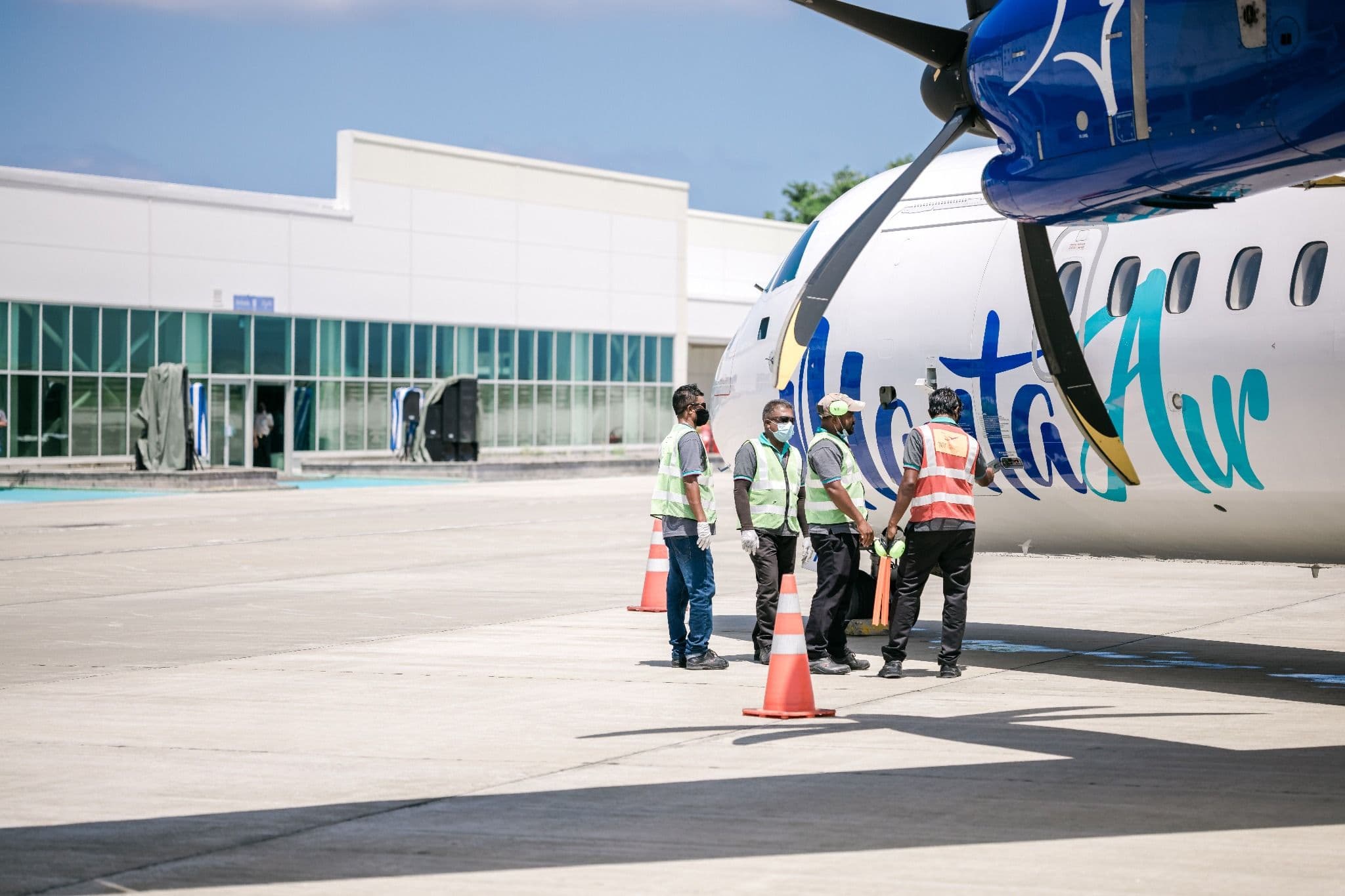 Ground crew standing beside a turboprop aircraft on an airport apron.