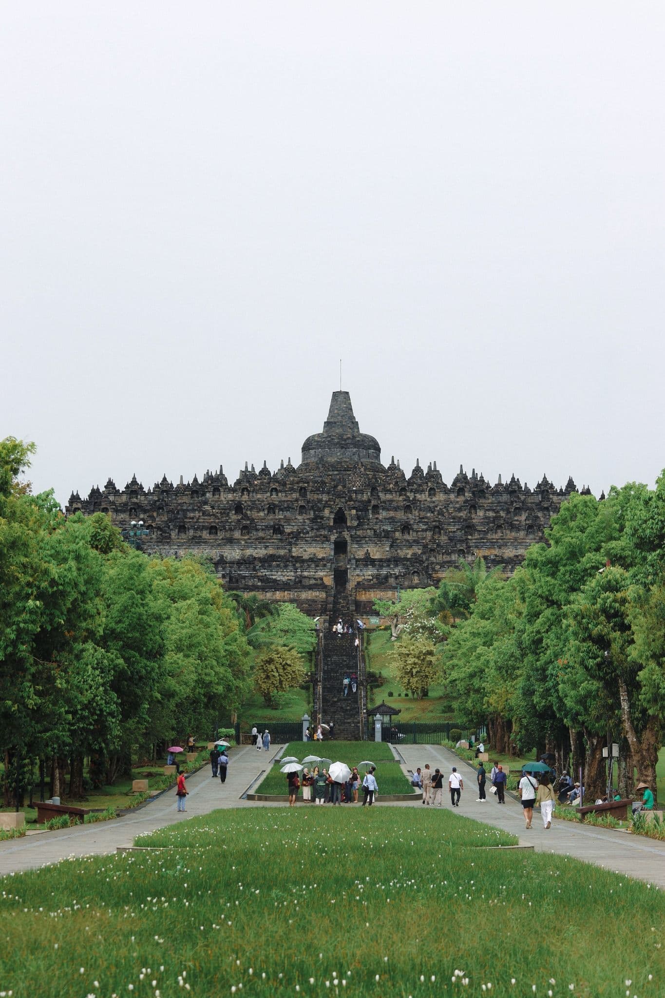 Borobudur Temple rising above green gardens with visitors walking toward the monument.