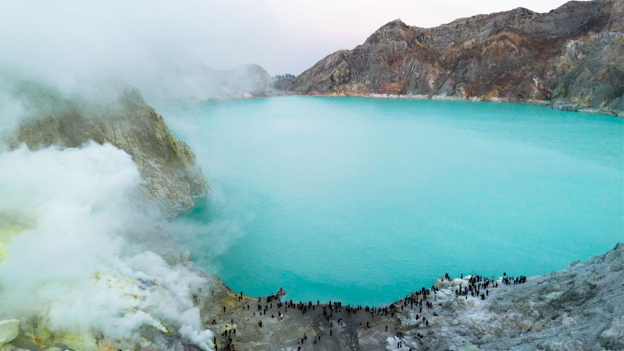 Turquoise crater lake at Ijen surrounded by volcanic ridges and rising sulfur mist
