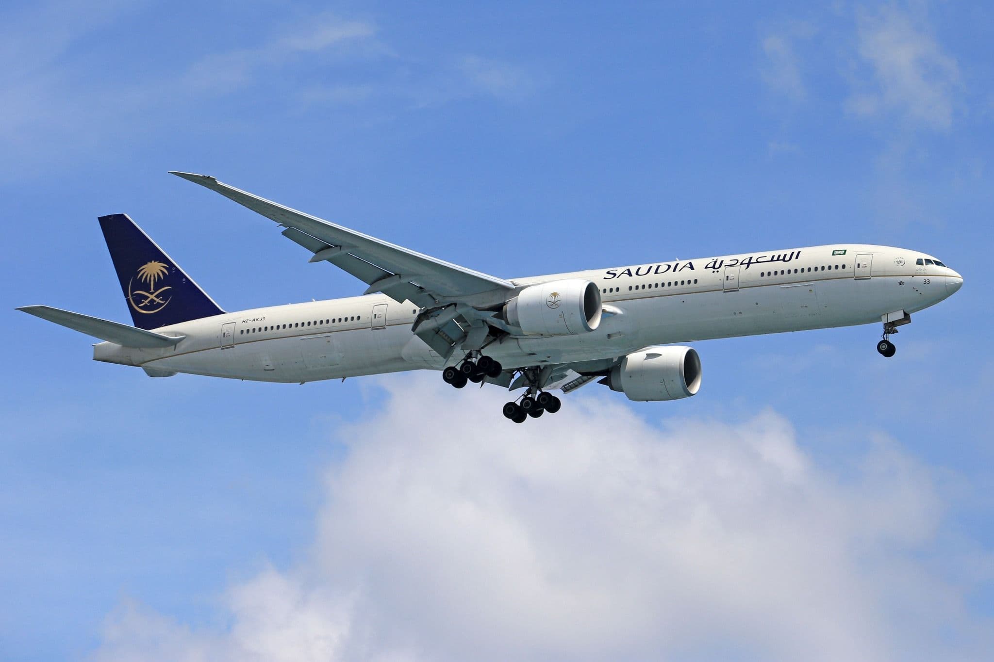 Saudia wide-body aircraft approaching with its landing gear down against a blue sky.